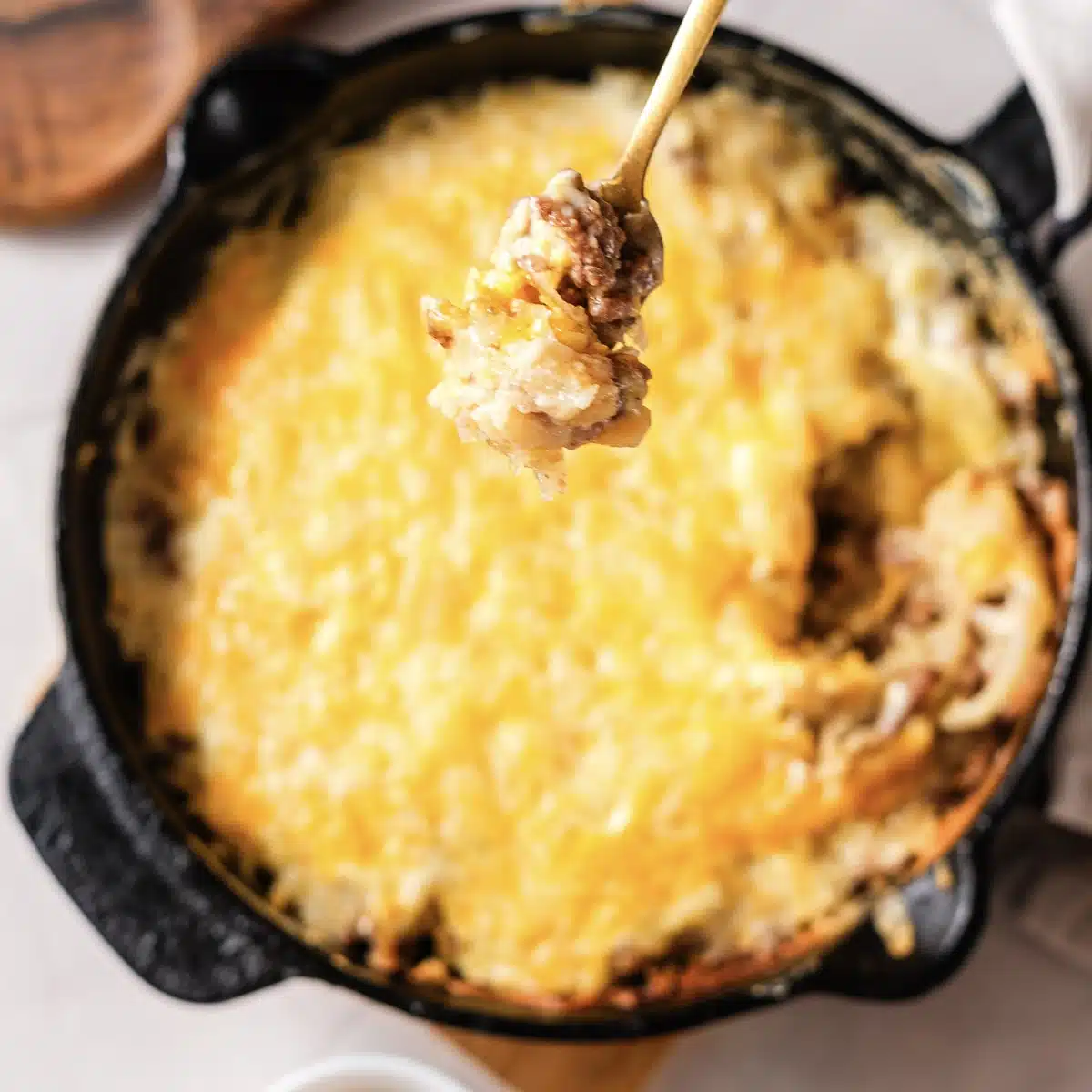 A hand lifting a spoonful of the cheesy bake from the skillet