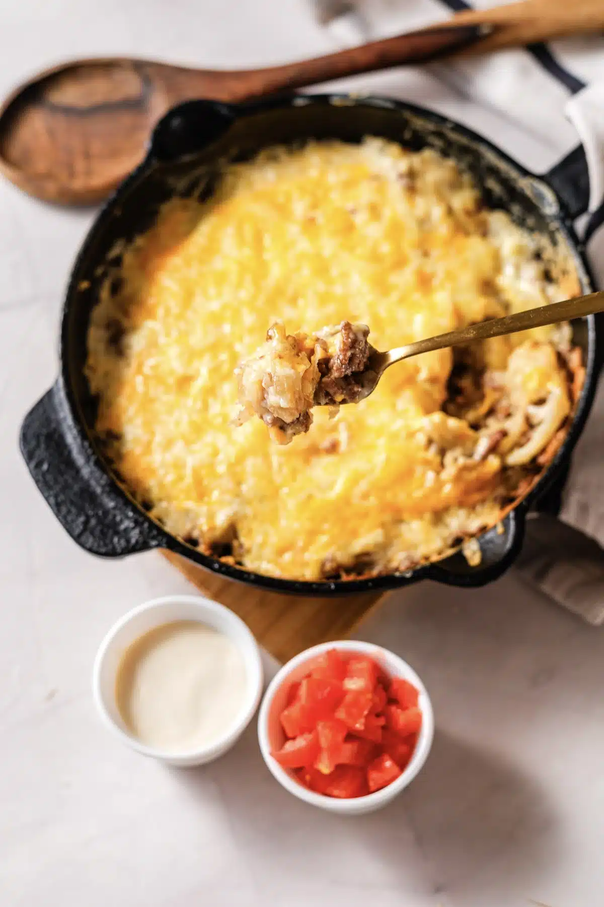 A gold spoon resting in the skillet with bowls of sour cream and diced tomato below