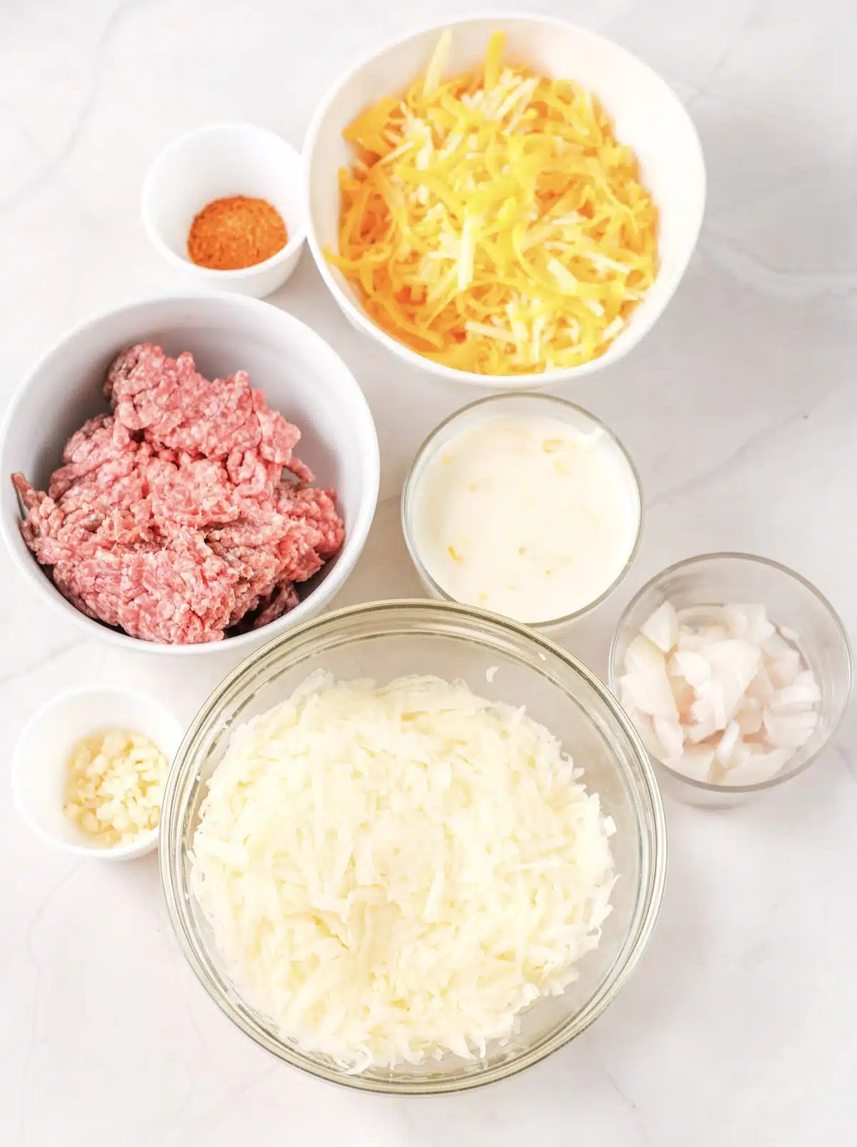Ingredients for taco hashbrown casserole: ground beef, taco seasoning, shredded hash browns, sour cream, shredded cheddar, onion and garlic