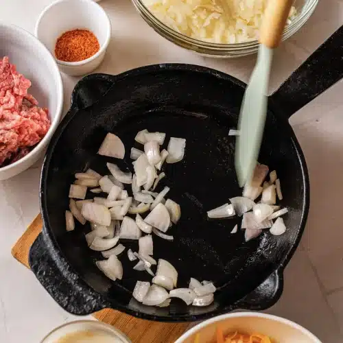 Diced onion cooking in a cast-iron skillet with a spatula