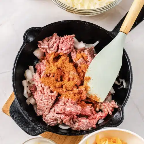 Taco seasoning sprinkled over the raw beef in the skillet