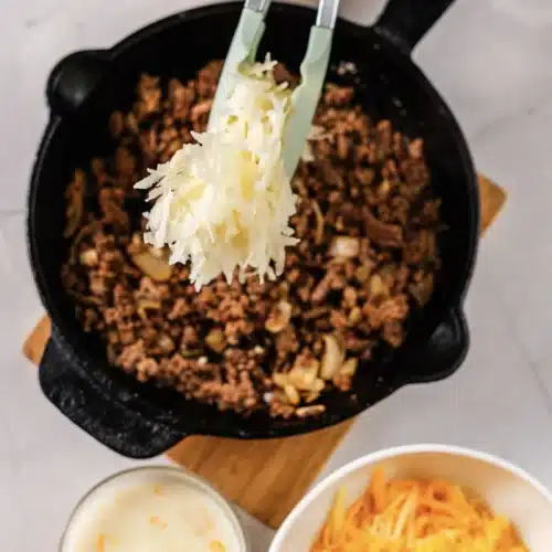 Shredded hash browns added to the beef with tongs