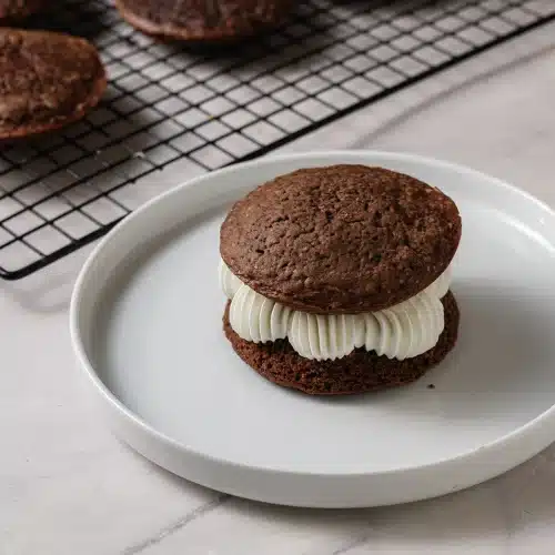 A finished whoopie pie on a white plate with the piped filling showing between the two cakes