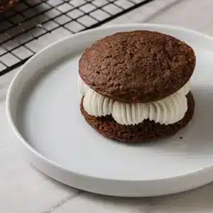 A single old-fashioned whoopie pie with piped vanilla filling on a white plate